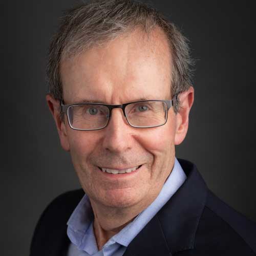 portrait of smiling man wearing glasses and light blue dress shirt below dark shirt